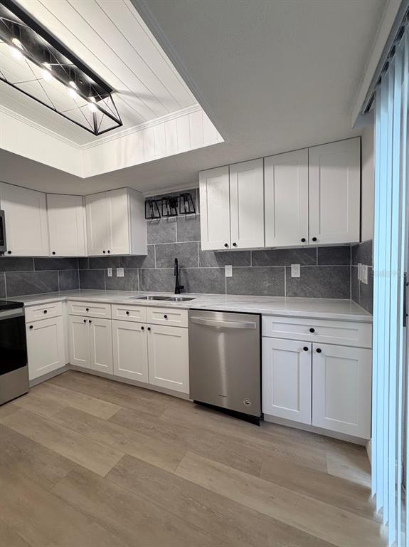 A kitchen features white cabinets, gray tile backsplash, stainless steel appliances, and wood-look flooring — 12406 EAGLESWOOD DRIVE UNIT B, HUDSON, FL