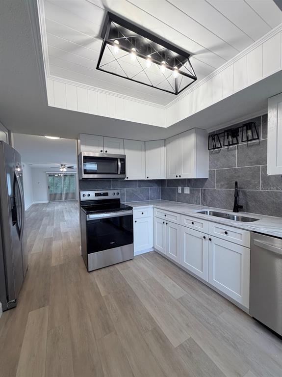 A kitchen features white cabinets, stainless steel appliances, gray tile backsplash, and a tray ceiling — 12406 EAGLESWOOD DRIVE UNIT B, HUDSON, FL