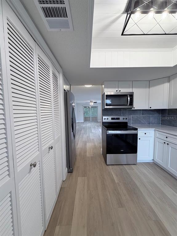 A kitchen with white cabinets, stainless steel appliances, and light wood-look flooring — 12406 EAGLESWOOD DRIVE UNIT B, HUDSON, FL