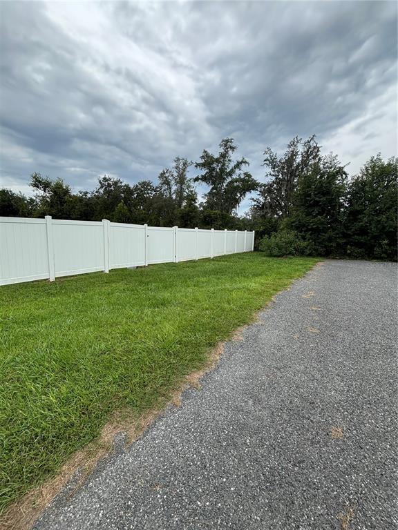 A white vinyl fence borders a grassy lawn next to a gravel driveway — SE 157TH STREET, SUMMERFIELD, FL