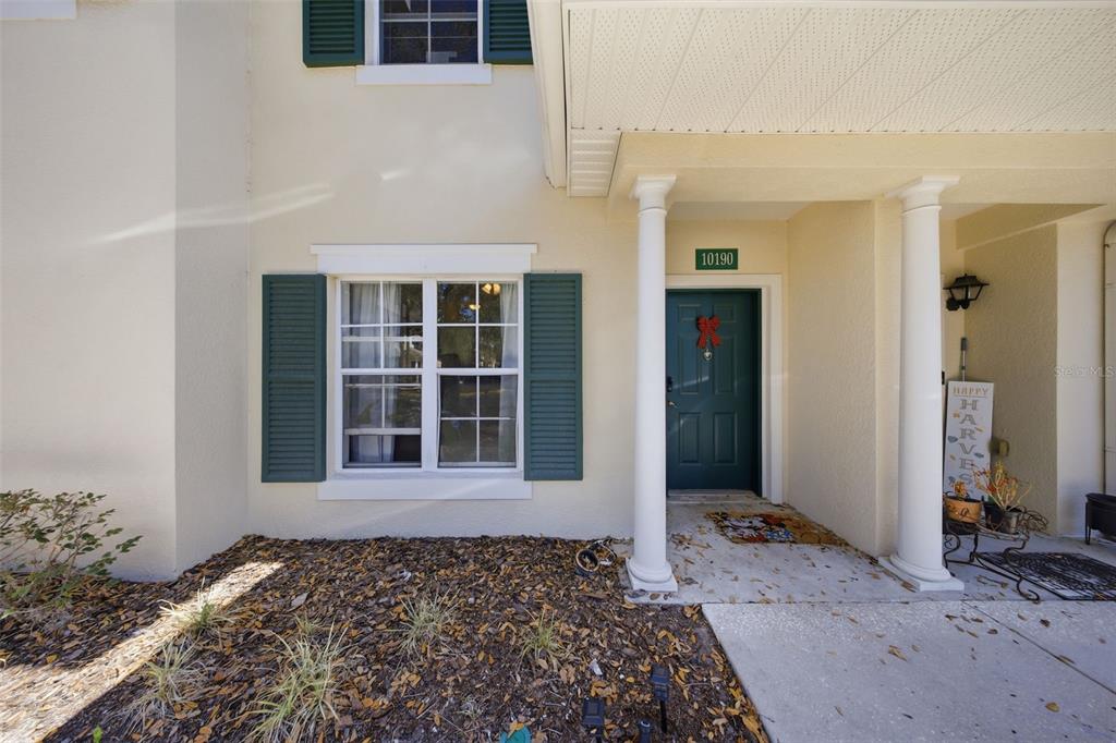A beige house exterior features a dark green front door, shutters, and a covered porch — 10190 REGENT PARK DRIVE UNIT 2103, ORLANDO, FL