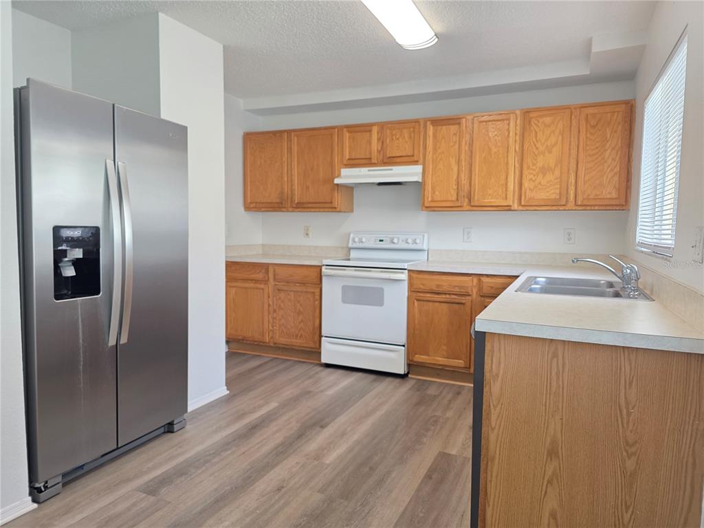 A kitchen features wood cabinets, white appliances, a stainless steel refrigerator, and wood-look flooring — 1410 OAKFORD COURT, BRANDON, FL
