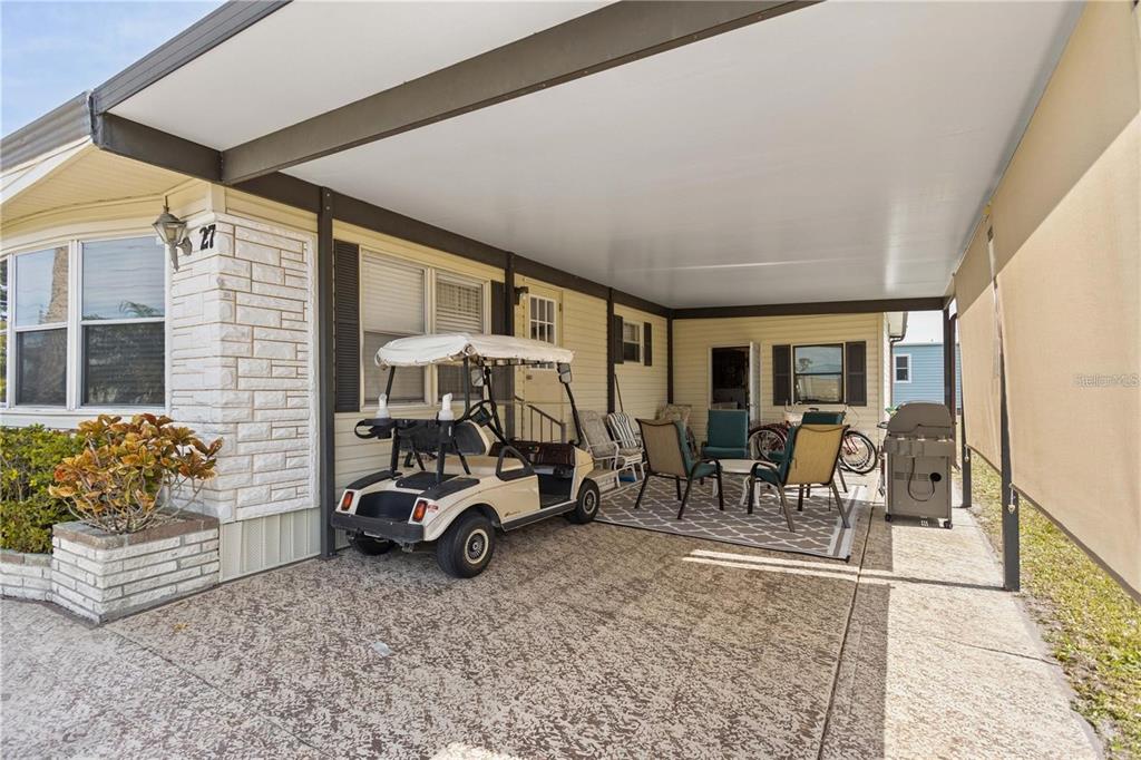 A covered carport features a golf cart, outdoor furniture, and a grill beside a house — 2100 KINGS HIGHWAY UNIT 27, PORT CHARLOTTE, FL