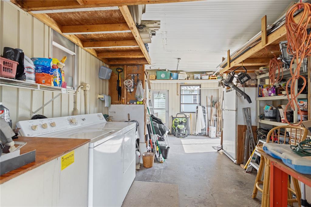 A garage space features a white laundry set, open wooden shelving, and concrete flooring — 2100 KINGS HIGHWAY UNIT 27, PORT CHARLOTTE, FL