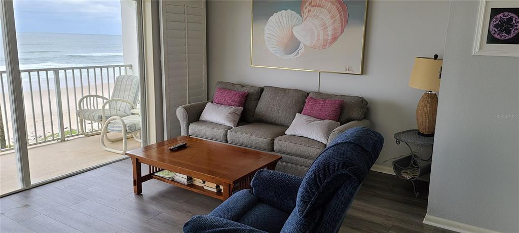 A living room features a gray sofa, blue recliner, and a balcony overlooking the ocean — 815 OCEAN SHORE BOULEVARD UNIT 12B, ORMOND BEACH, FL