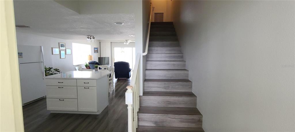 A staircase with wood-look flooring leads upward next to a kitchen with a white island — 815 OCEAN SHORE BOULEVARD UNIT 12B, ORMOND BEACH, FL