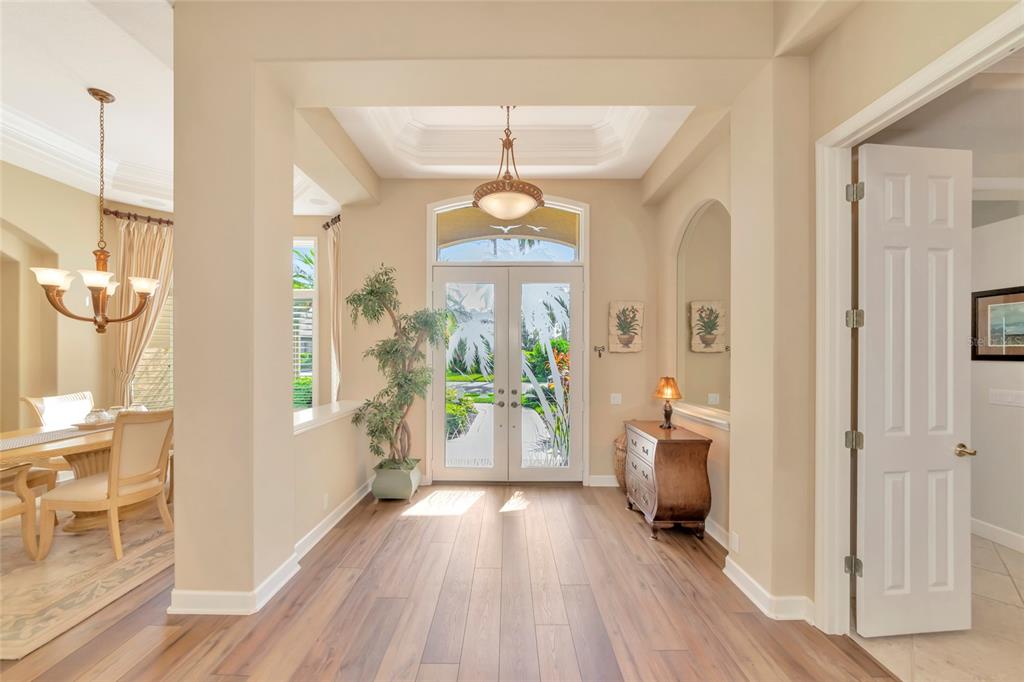 A bright foyer features wood-look flooring, a double-door entrance, and a tray ceiling with lighting — 4834 88TH STREET E, BRADENTON, FL