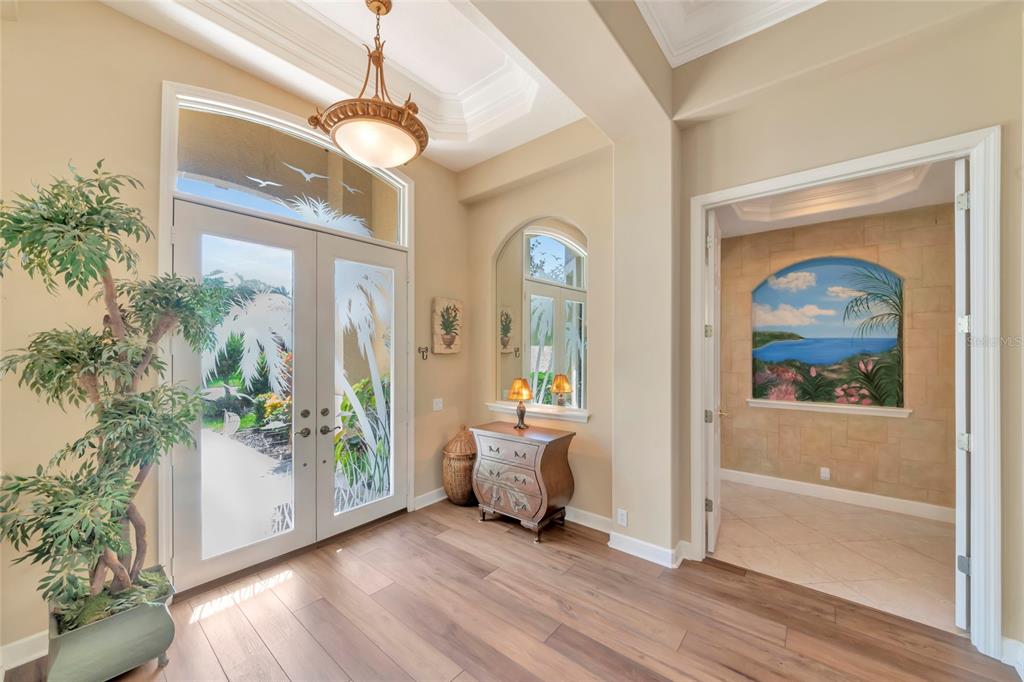An entryway features wood-look flooring, a double glass door, a chandelier, and a painted mural — 4834 88TH STREET E, BRADENTON, FL