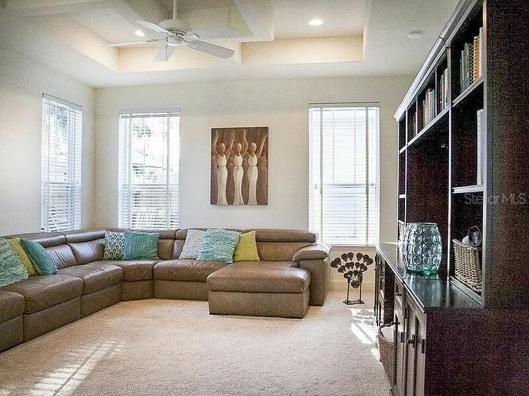 A living room features a large brown sectional sofa, a built-in bookshelf, and tray ceilings — 250 KILLARNEY, WINTER PARK, FL