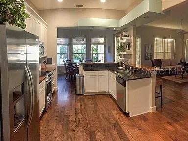 A kitchen with white cabinets, stainless steel appliances, and hardwood floors opens to a dining area — 250 KILLARNEY, WINTER PARK, FL