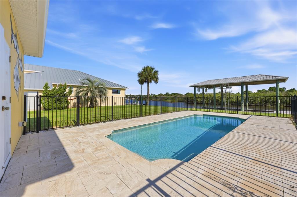 A backyard swimming pool with a stone patio, black metal fence, and a boat dock — 342 N 12TH STREET, FLAGLER BEACH, FL