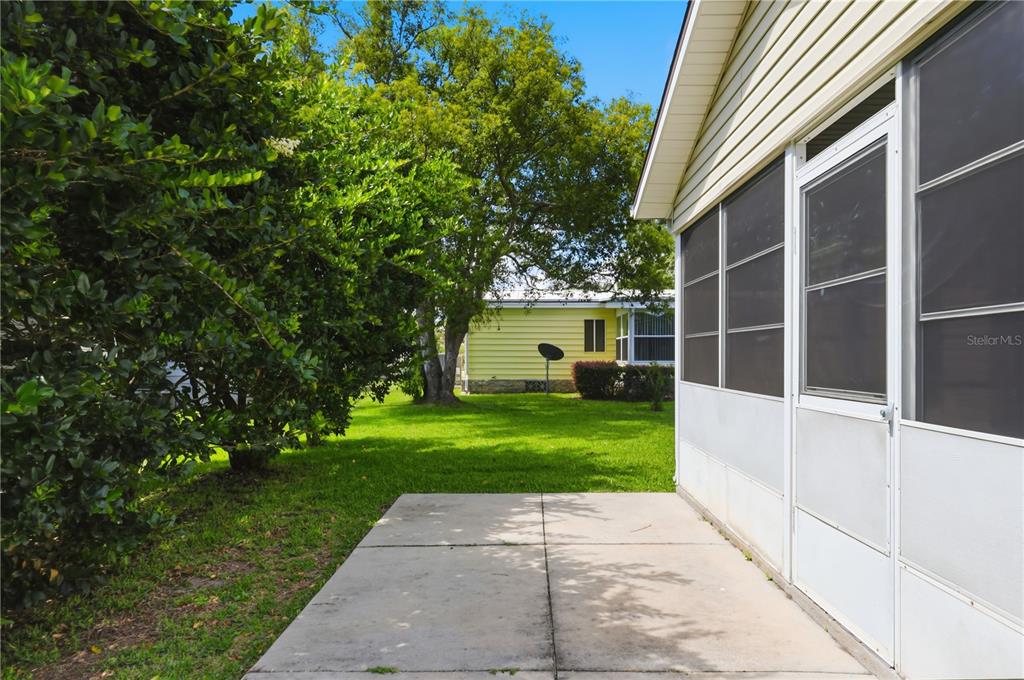 A concrete patio sits beside a screened-in porch with a grassy yard and trees beyond — 25110 BELLEVUE, LEESBURG, FL