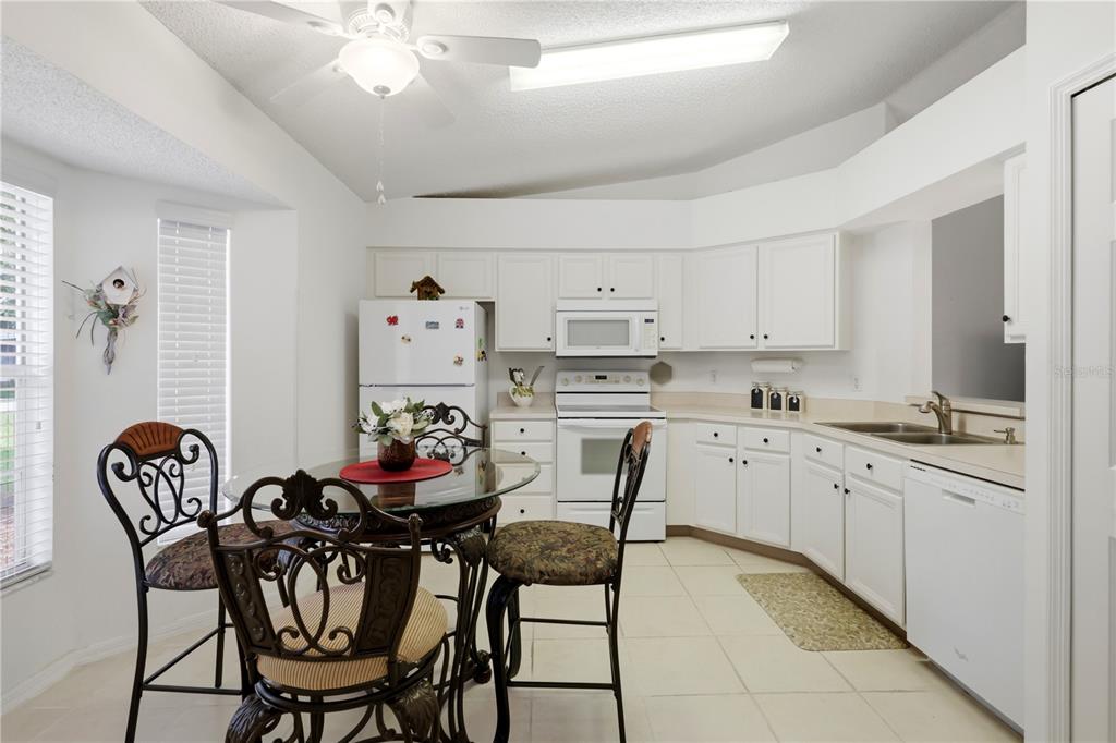A kitchen with white cabinets, white appliances, and a glass-topped dining table with chairs — 25110 BELLEVUE, LEESBURG, FL