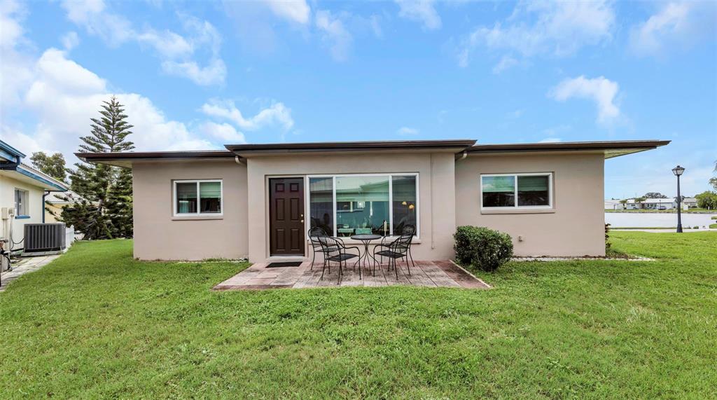 A single-story house exterior features a beige facade, a small patio, and a grassy yard — 5355 FERNDALE PLACE N, PINELLAS PARK, FL