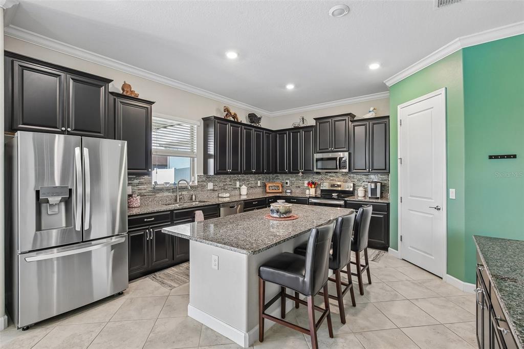 A kitchen with dark cabinets, granite countertops, and an island, adjacent to a dining area — 11705 NAVAJO SANDSTONE STREET, RIVERVIEW, FL