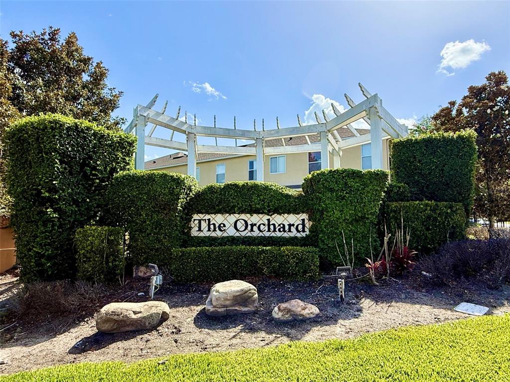 A white pergola structure sits behind a hedge sign reading The Orchard in front of buildings — 218 WINTER NELLIS CIRCLE, WINTER GARDEN, FL