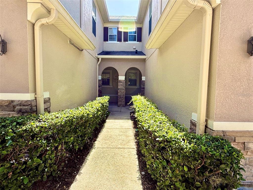 A concrete walkway leads between two hedges toward the entrance of a two-story building — 218 WINTER NELLIS CIRCLE, WINTER GARDEN, FL