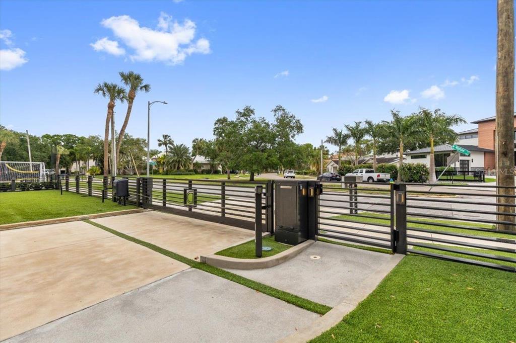 A metal sliding gate opens to a paved driveway and a street with palm trees — 5131 W NEPTUNE WAY, TAMPA, FL