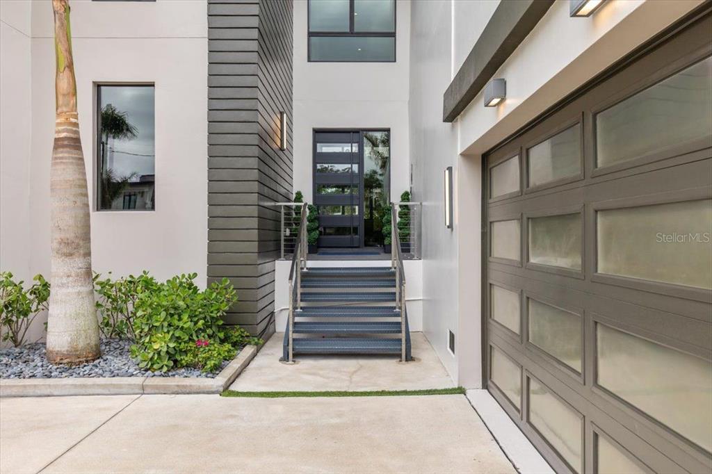 A modern home exterior features a dark metal staircase leading to a glass-paneled front door — 5131 W NEPTUNE WAY, TAMPA, FL