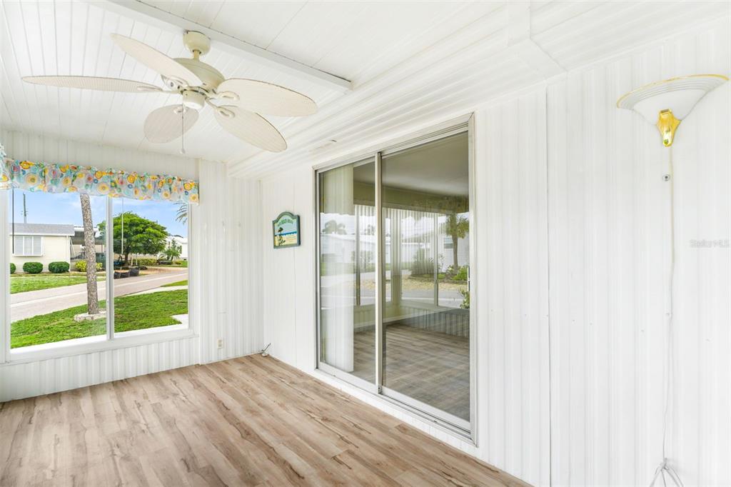 A sunroom with wood-look flooring, a ceiling fan, sliding glass doors, and white paneled walls — 822 BOGIE, VENICE, FL