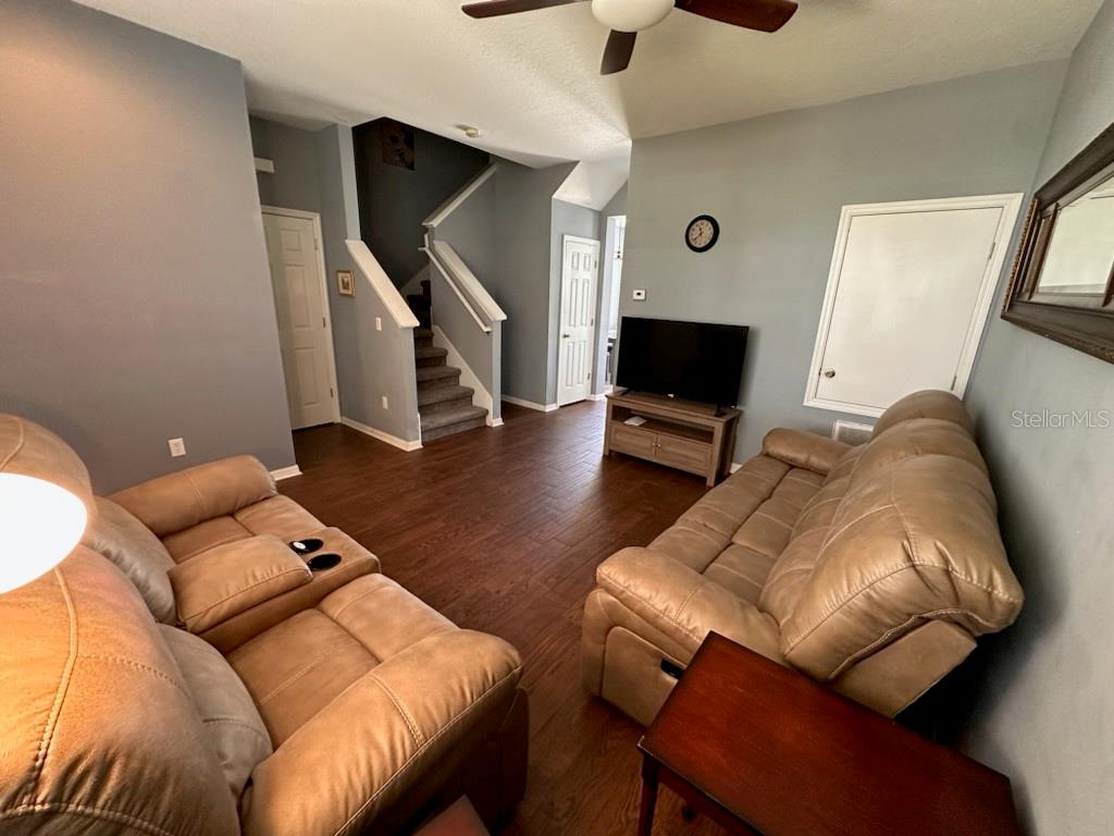 A living room features wood-look flooring, two tan sofas, a television, and a staircase — 8524 DANFORTH DRIVE, WINDERMERE, FL