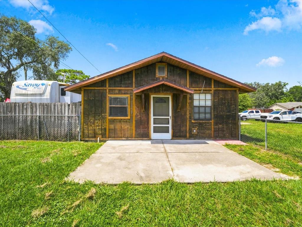 A small, wood-sided house with a concrete patio sits in a grassy yard — 12823 BUCKEYE DRIVE, HUDSON, FL