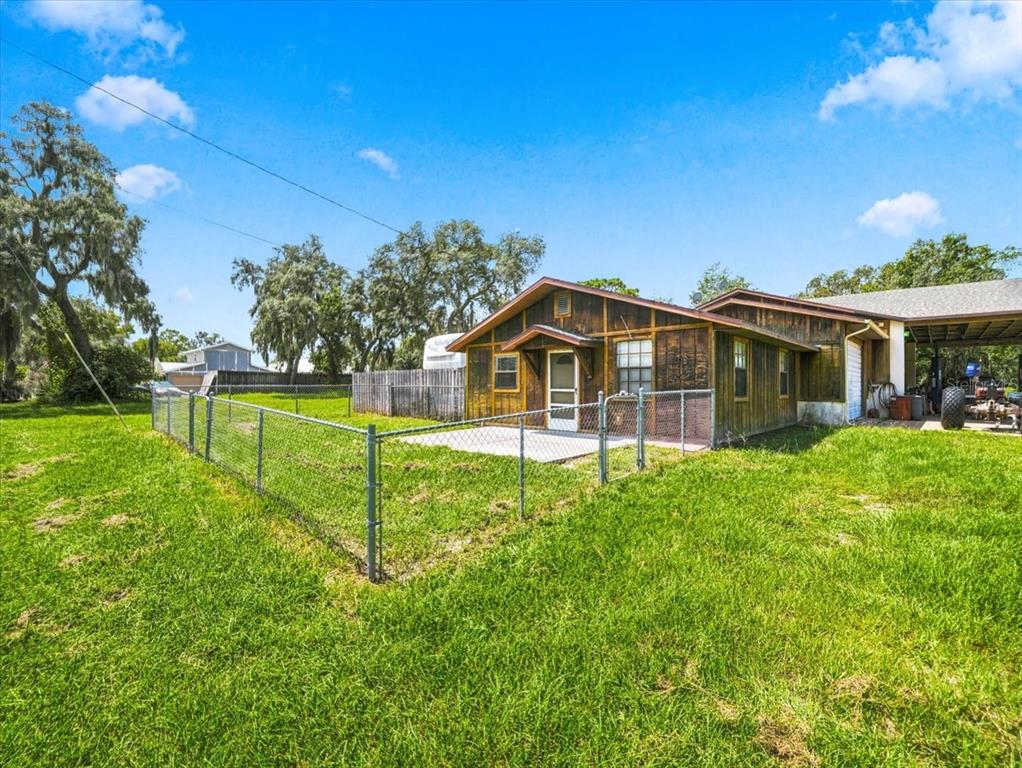 A wooden house with a fenced patio sits on a grassy lot under a blue sky — 12823 BUCKEYE DRIVE, HUDSON, FL