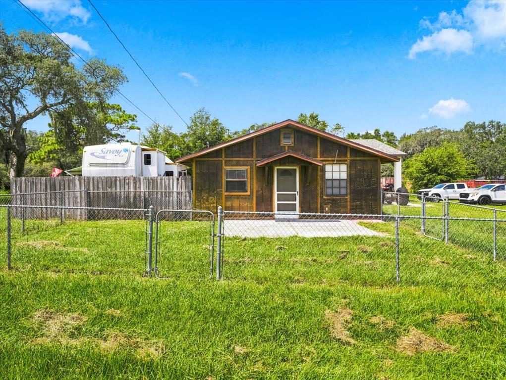 A small, brown wooden house with a front porch stands behind a chain-link fence — 12823 BUCKEYE DRIVE, HUDSON, FL