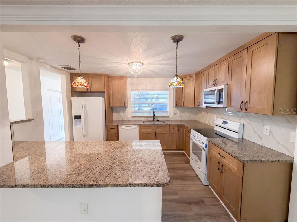 A kitchen features light wood cabinets, granite countertops, a white refrigerator, and two stained-glass pendants — 5122 BAY BOULEVARD, PORT RICHEY, FL