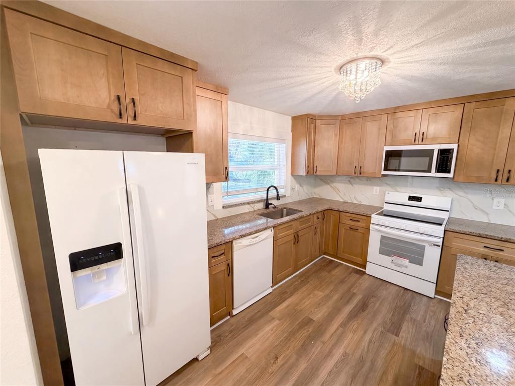 A kitchen features light wood cabinets, white appliances, granite countertops, and wood-look flooring — 5122 BAY BOULEVARD, PORT RICHEY, FL