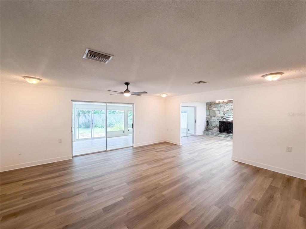 A living room with wood-look flooring, a ceiling fan, sliding glass doors, and a stone fireplace — 5122 BAY BOULEVARD, PORT RICHEY, FL