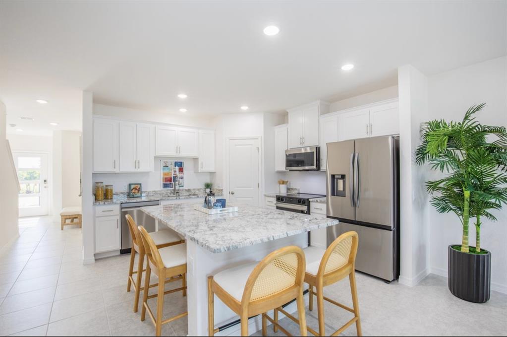 A bright kitchen features white cabinets, granite countertops, a central island, and stainless steel appliances — 10721 FOUNTAIN PALM CIRCLE, BOKEELIA, FL