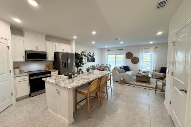 An open-concept kitchen and living area features white cabinetry, a granite island, and tile flooring — 10721 FOUNTAIN PALM CIRCLE, BOKEELIA, FL