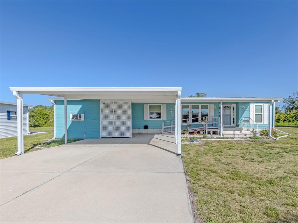 A light blue single-story house features a white carport and a concrete driveway — 592 PORTSIDE DRIVE, NORTH PORT, FL