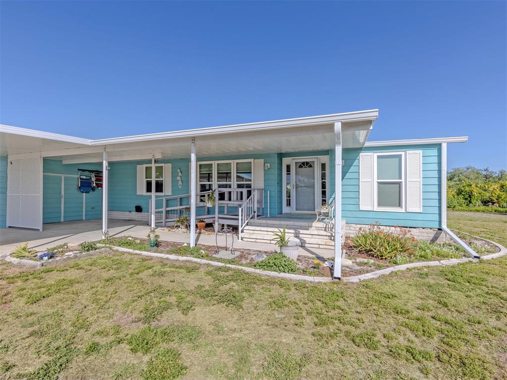 A light blue manufactured home features a covered carport, a front porch, and white shutters — 592 PORTSIDE DRIVE, NORTH PORT, FL