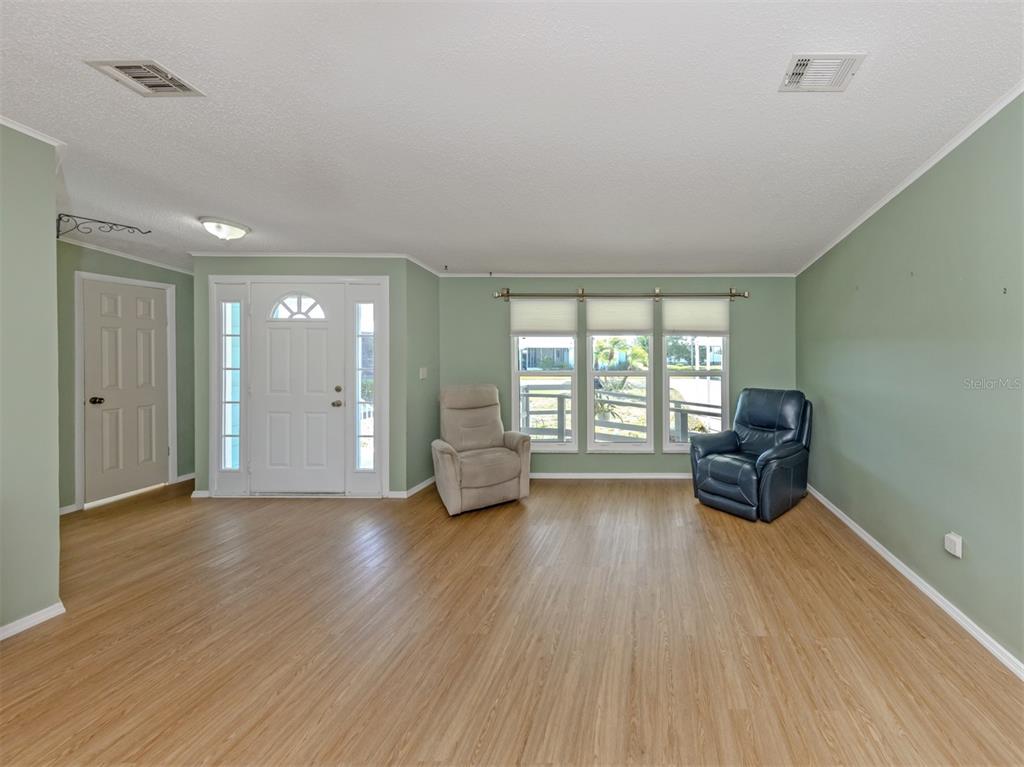 A living room with light green walls, wood-look flooring, a front door, and two recliners — 592 PORTSIDE DRIVE, NORTH PORT, FL