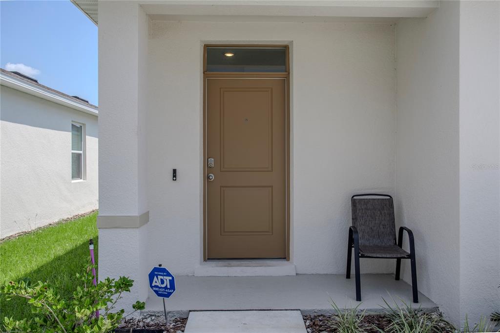 A tan front door with a transom window sits on a covered concrete porch — 191 AMBERWOOD WAY, UMATILLA, FL