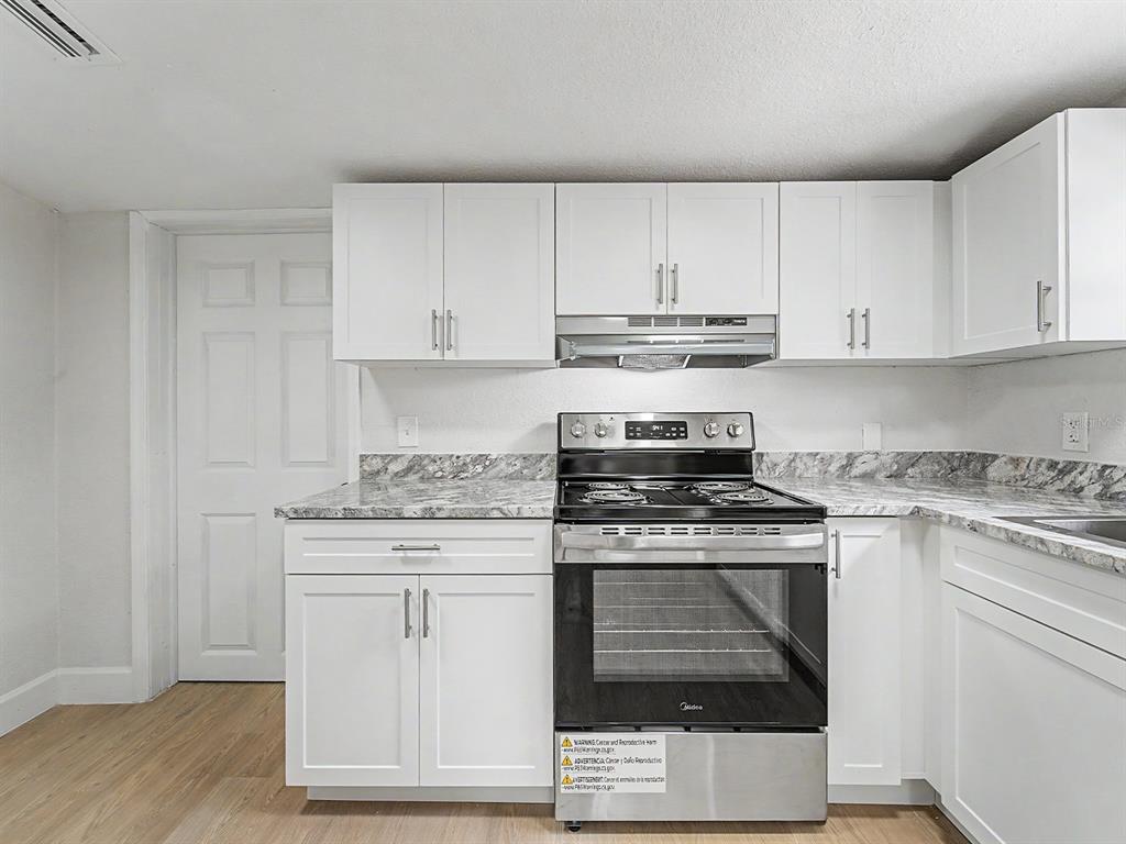 A kitchen features white cabinets, a stainless steel stove, and a gray marble-patterned countertop — 8117 N KLONDYKE STREET, TAMPA, FL