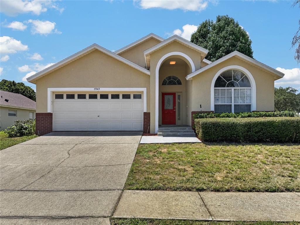 A tan single-story house features a red front door, arched entryway, and a two-car garage — 15943 HERON HILL STREET, CLERMONT, FL