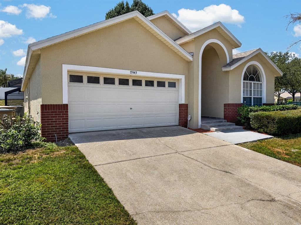 A single-story house features a tan stucco exterior, a two-car garage, and an arched entryway — 15943 HERON HILL STREET, CLERMONT, FL