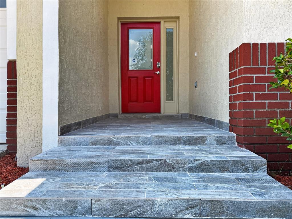 A red front door with a side window is accessed by stone-tiled steps — 15943 HERON HILL STREET, CLERMONT, FL