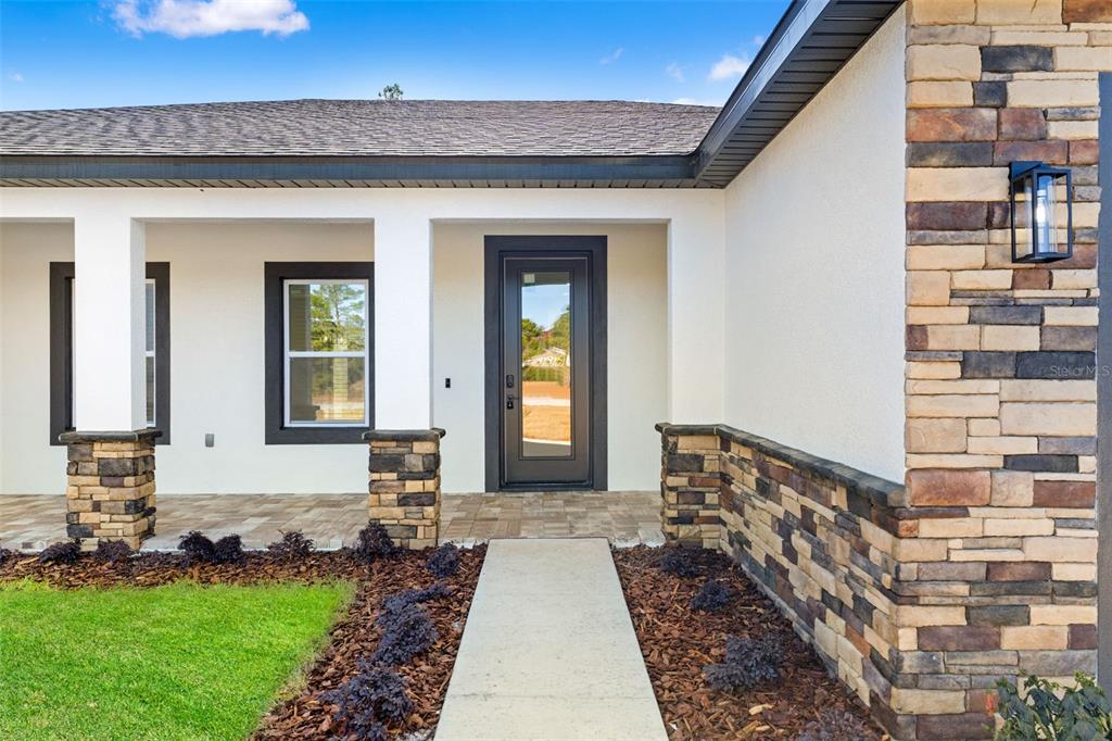 The exterior of a house features a stone-accented facade, a glass-paneled front door, and landscaping — 10439 GYPSY AVENUE, WEEKI WACHEE, FL