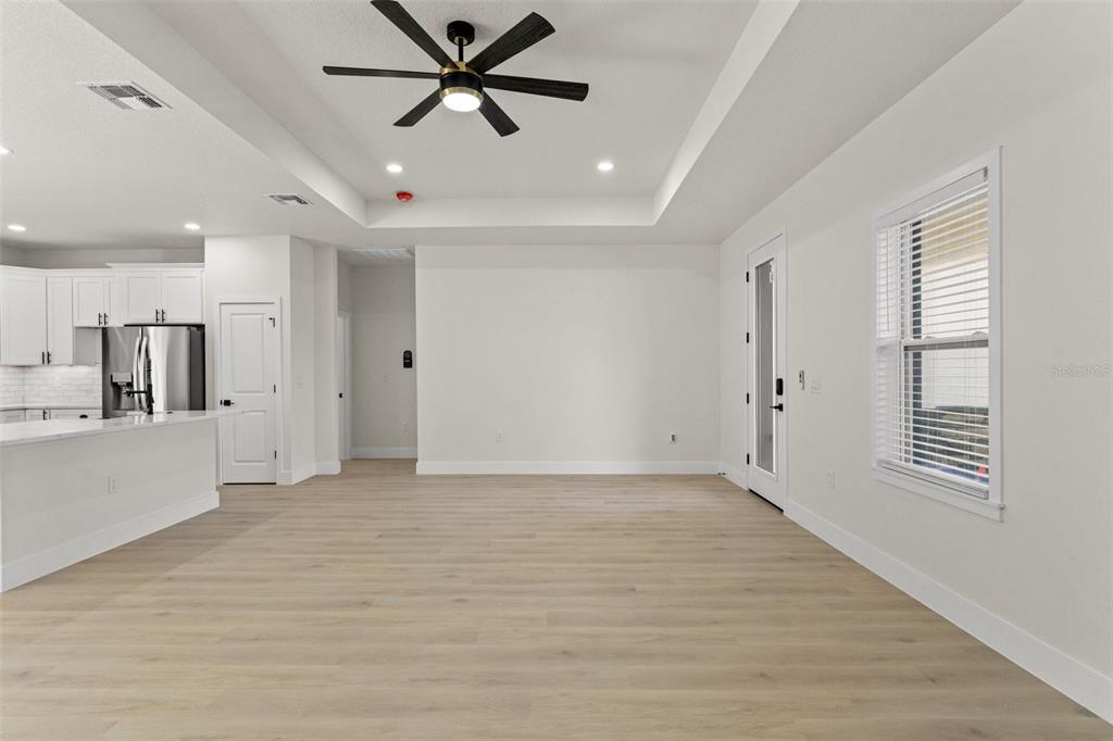 An open-concept living area features light wood flooring, a tray ceiling, and a ceiling fan — 10439 GYPSY AVENUE, WEEKI WACHEE, FL