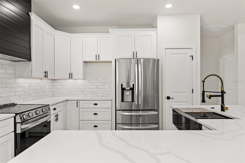 A modern kitchen features white cabinets, stainless steel appliances, and a white quartz island countertop — 10439 GYPSY AVENUE, WEEKI WACHEE, FL