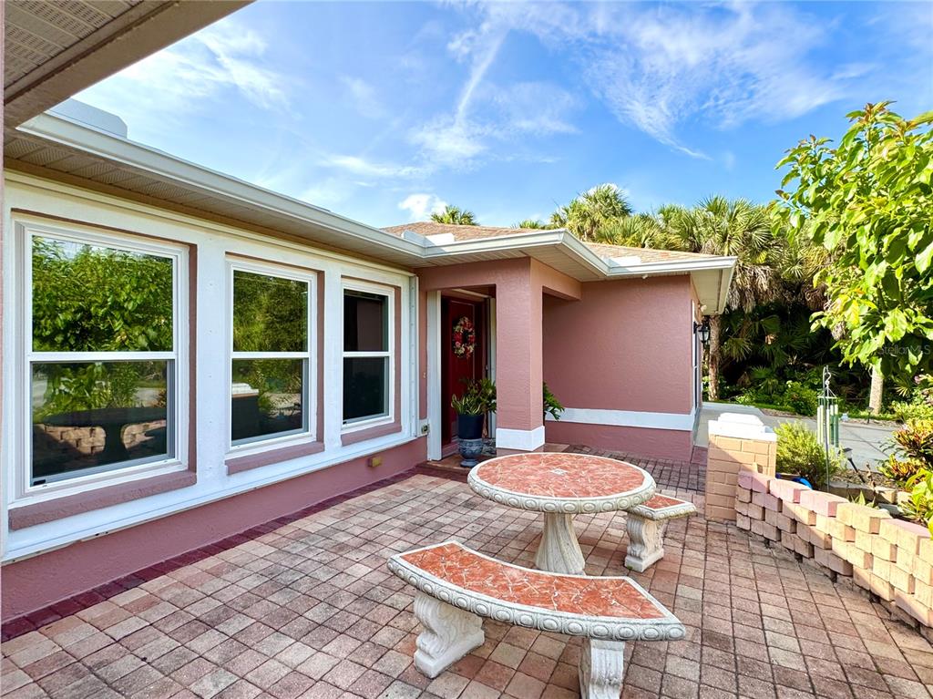 A patio with a stone table and benches sits outside a pink house with windows — 4353 BOYER TERRACE, NORTH PORT, FL