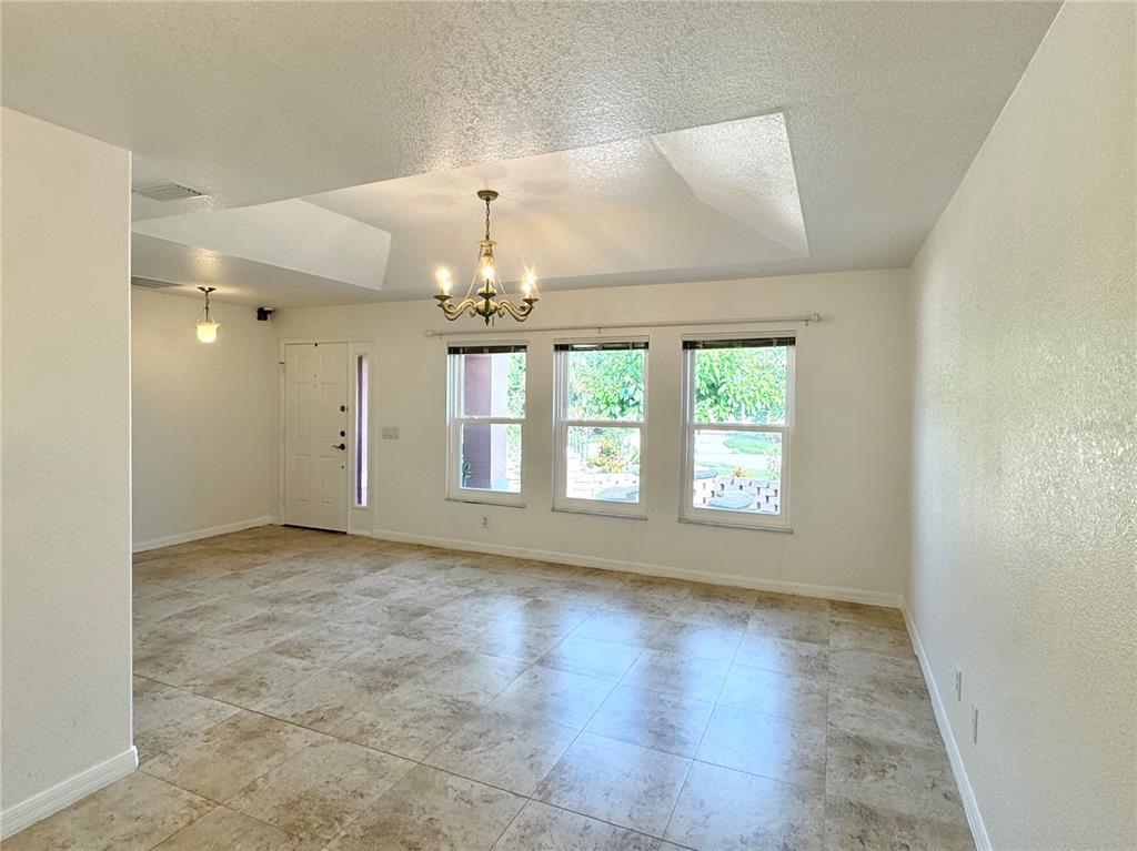 A bright, empty room features tiled flooring, a tray ceiling with a chandelier, and three windows — 4353 BOYER TERRACE, NORTH PORT, FL