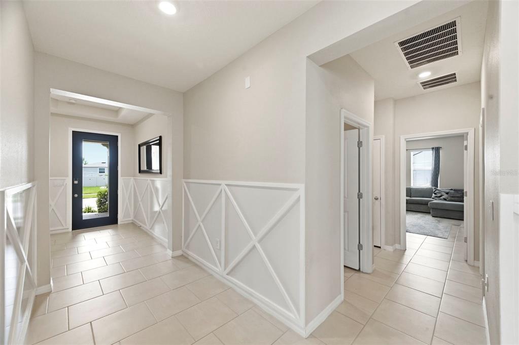 A bright entryway features light tile flooring and white walls with decorative X-pattern wainscoting — 10403 LAXER CAY LOOP, SAN ANTONIO, FL