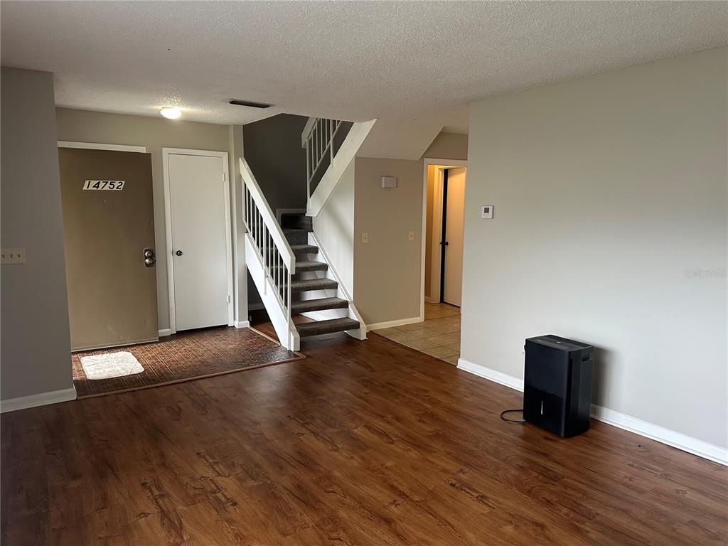 An interior view shows a living area with wood-look flooring, a staircase, and an entryway — 14752 MORNING DRIVE, LUTZ, FL