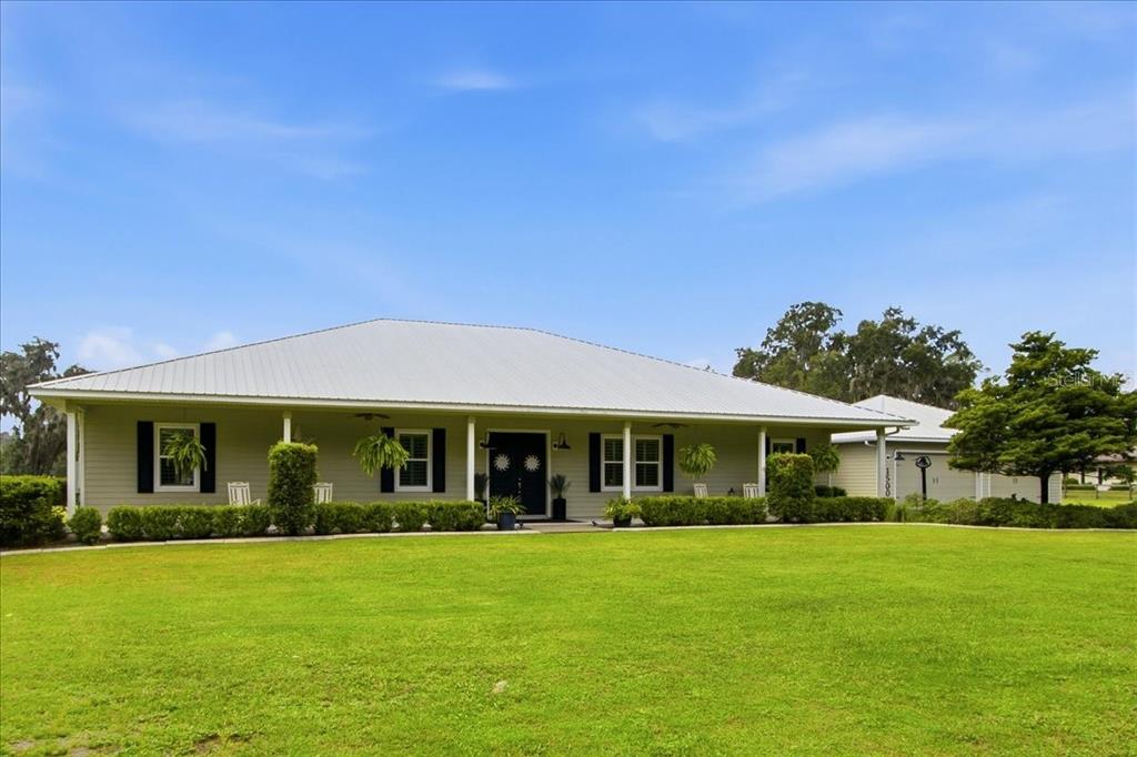 A single-story house with a metal roof and a wide front porch sits on a lawn — 1500 SPRING GARDEN RANCH ROAD, DE LEON SPRINGS, FL