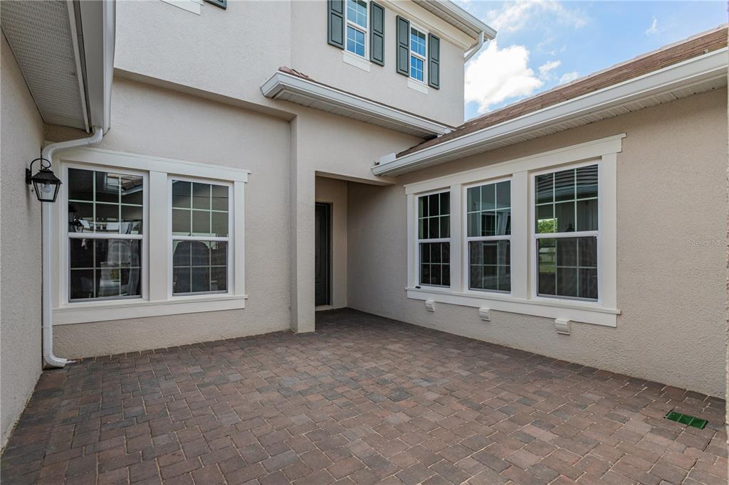 A paved courtyard sits between two sections of a beige house with white-trimmed windows — 10176 BROCKSPORT CIRCLE, GOTHA, FL